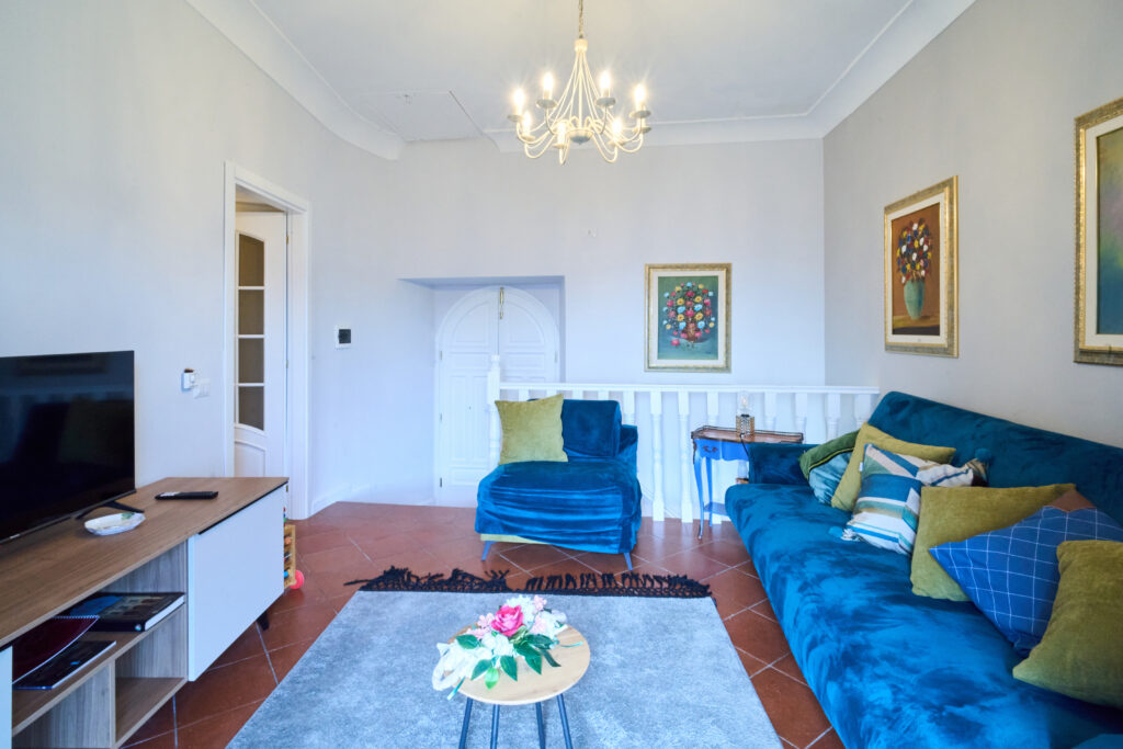 Salotto con divano blu, poltrona, televisore su un mobile in legno e lampadario