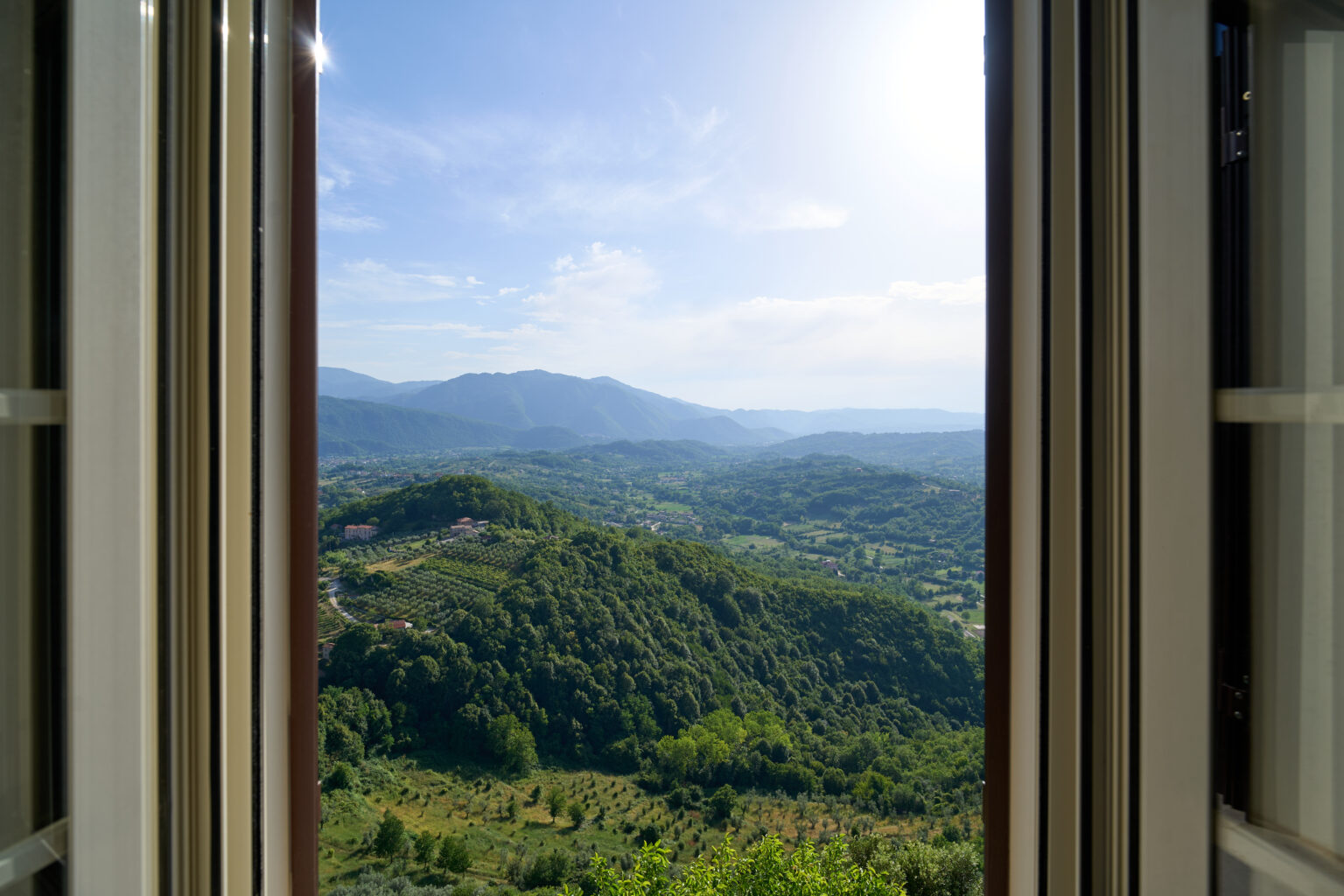 Vista sulla valle e sui boschi da una finestra con le imposte aperte