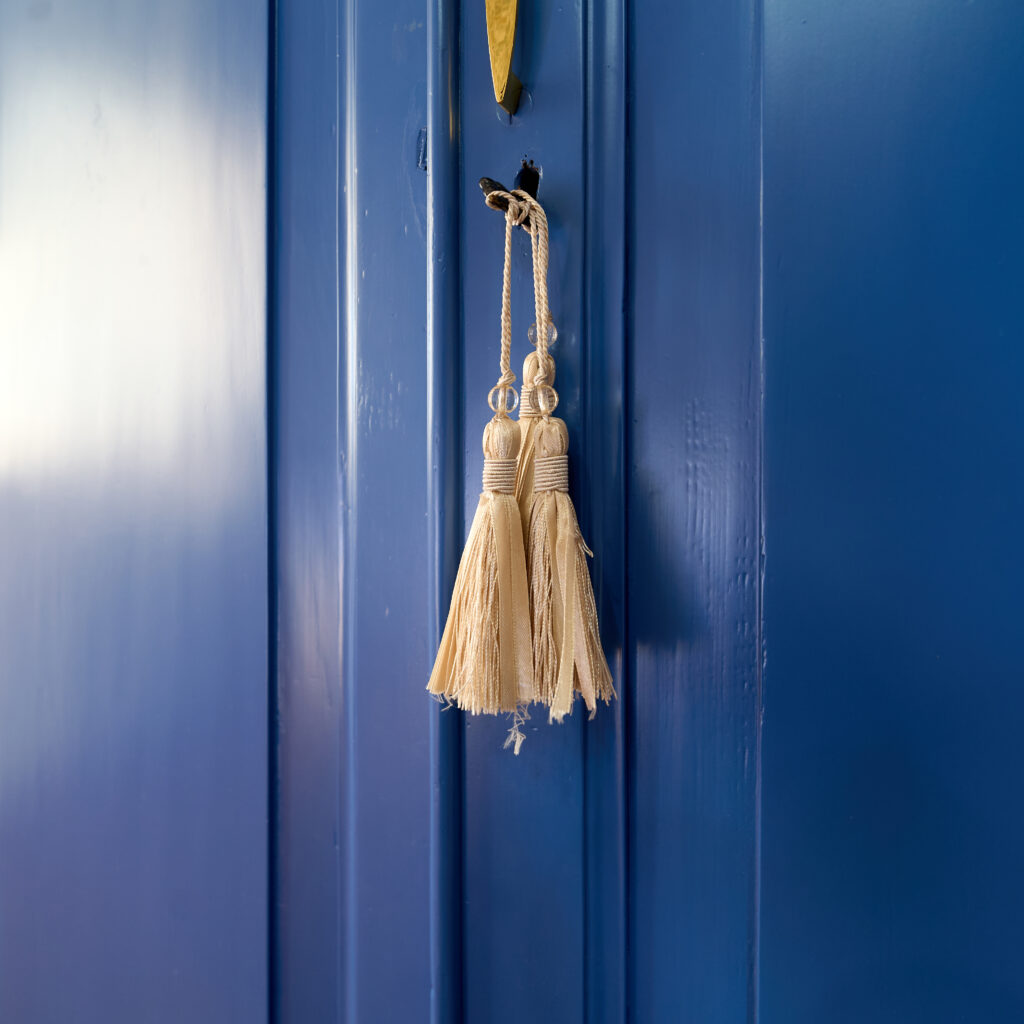 Chiave con nappa color panna appesa a un portone blu