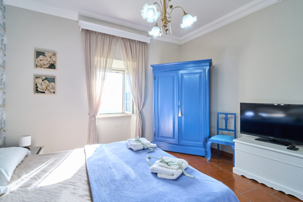 Camera matrimoniale con armadio azzurro, televisore e letto con copriletto blu