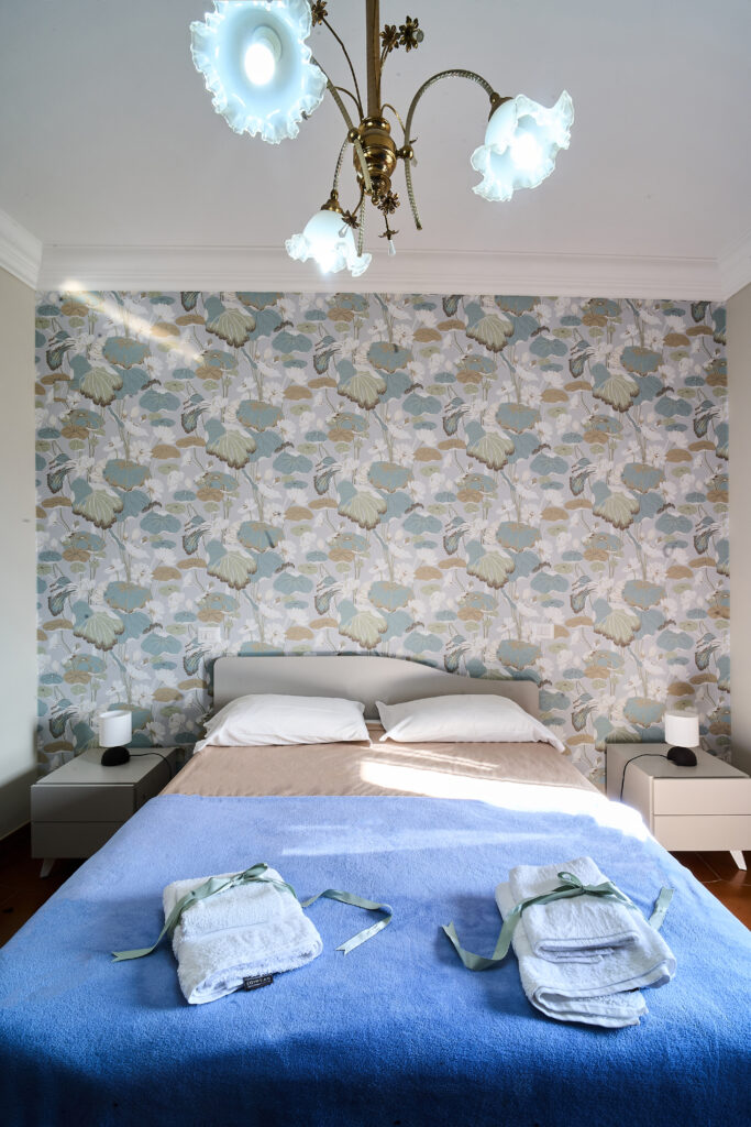 Letto matrimoniale con copriletto blu e carta da parati a fiori alla testata