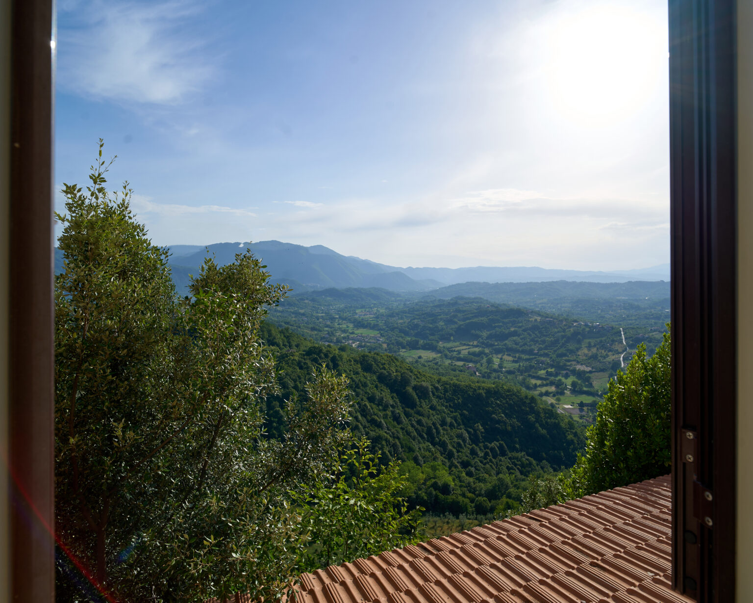 Vista della Valle di Comino e delle montagne da una finestra, con i tetti in cotto in primo piano