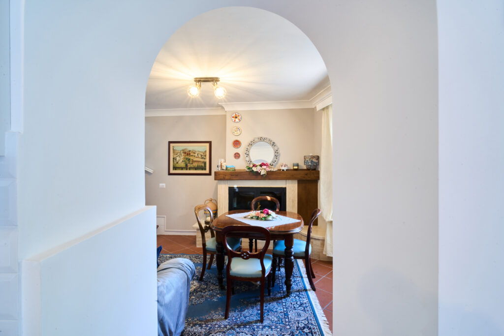 Soggiorno con tavolo e sedie e camino, visto attraverso un arco